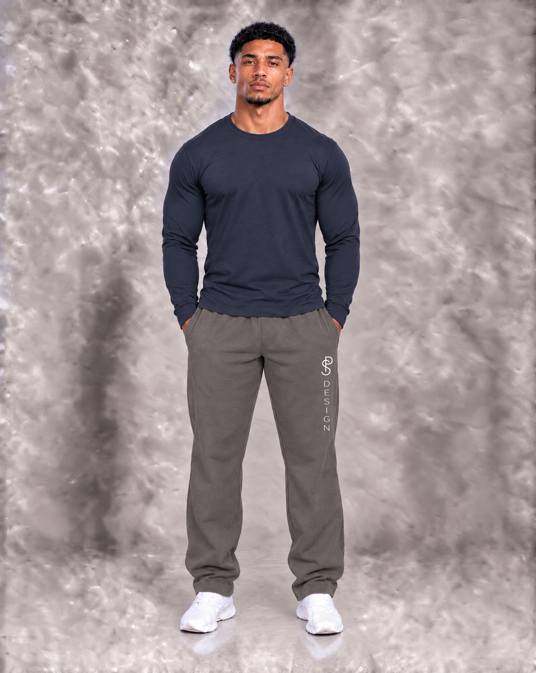 Paul Samuel Design Core Motion Sweatpants in Iron Moss, full-front view on athletic male model wearing a navy long-sleeve shirt, featuring relaxed athletic fit and vertical PS DESIGN branding.